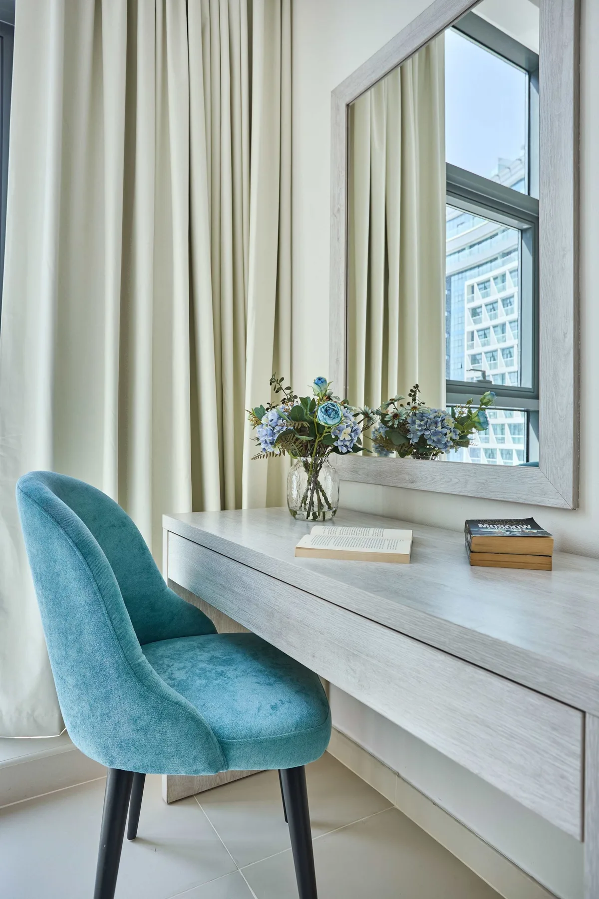Un escritorio y un asiento tapizado están junto a una gran ventana con cortinas.