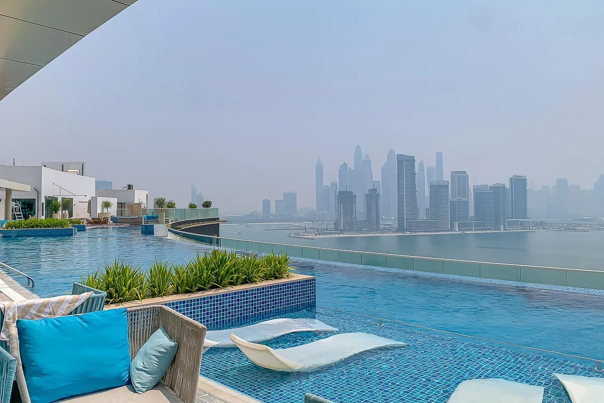 Una piscina en la azotea mira hacia un horizonte urbano brumoso, con asientos acolchados junto al agua.