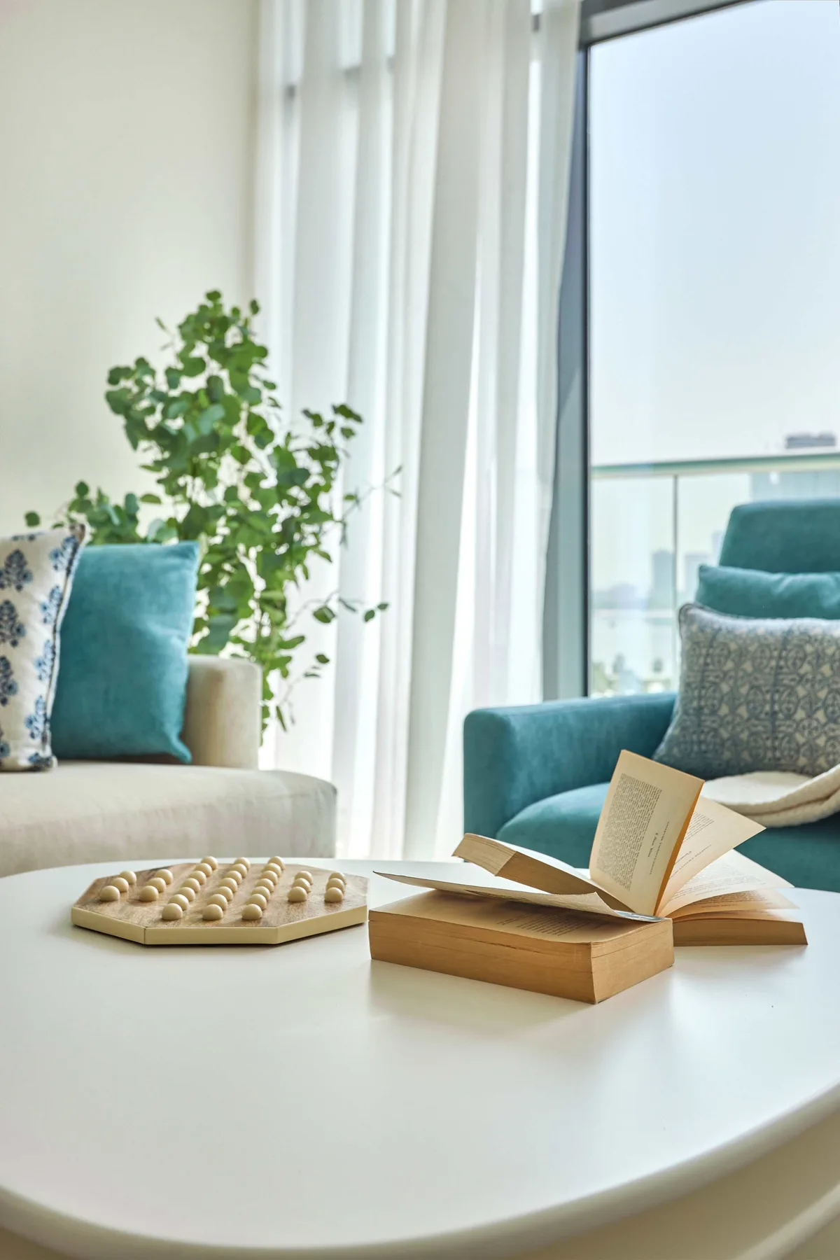 Una sala luminosa con asientos turquesa, una planta y un libro abierto sobre una mesa.