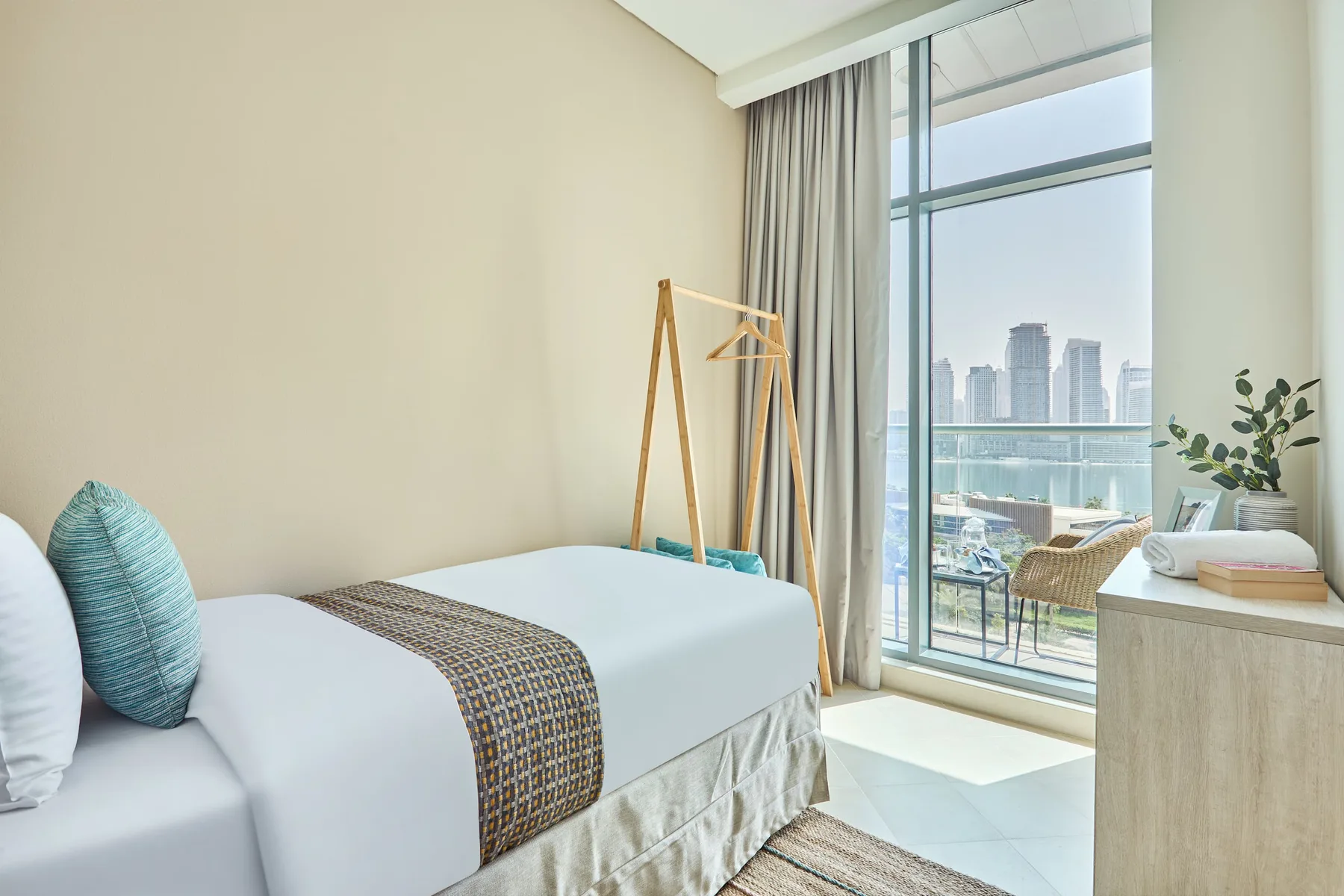 Un dormitorio luminoso con una cama junto a una ventana de piso a techo con vistas a la ciudad.