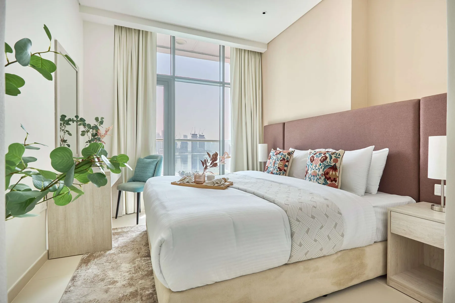 Un dormitorio luminoso con una cama tendida, cortinas claras y una ventana amplia.