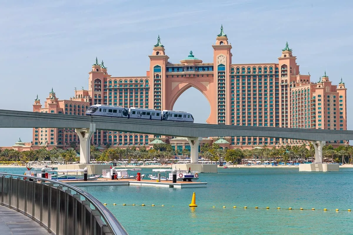 Un gran hotel frente al agua se alza detrás de una vía elevada y aguas turquesas.
