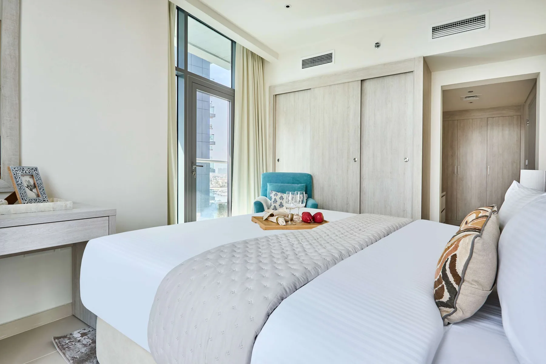 Un dormitorio luminoso con dos camas, una ventana grande y armarios claros.