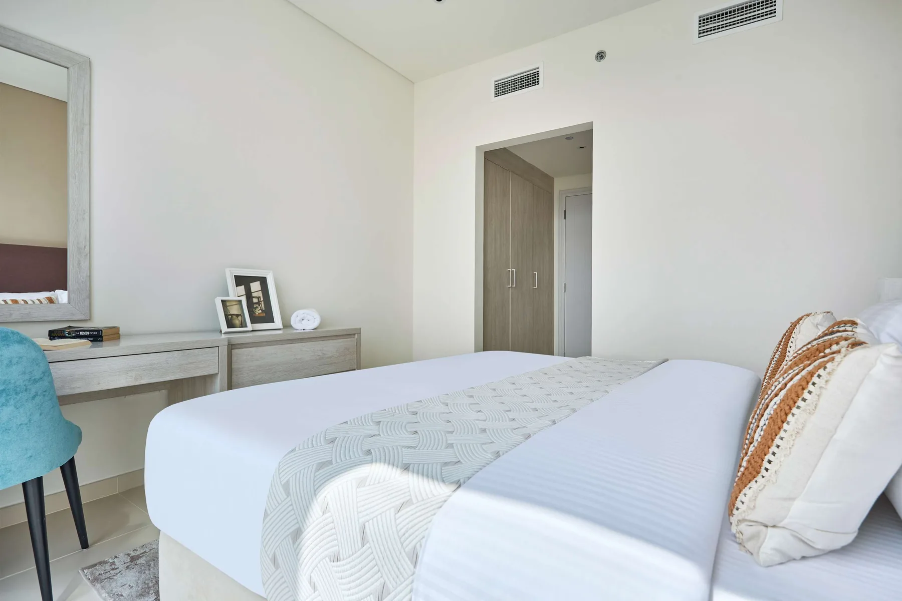 Un dormitorio luminoso con una cama tendida y un escritorio junto a la pared.
