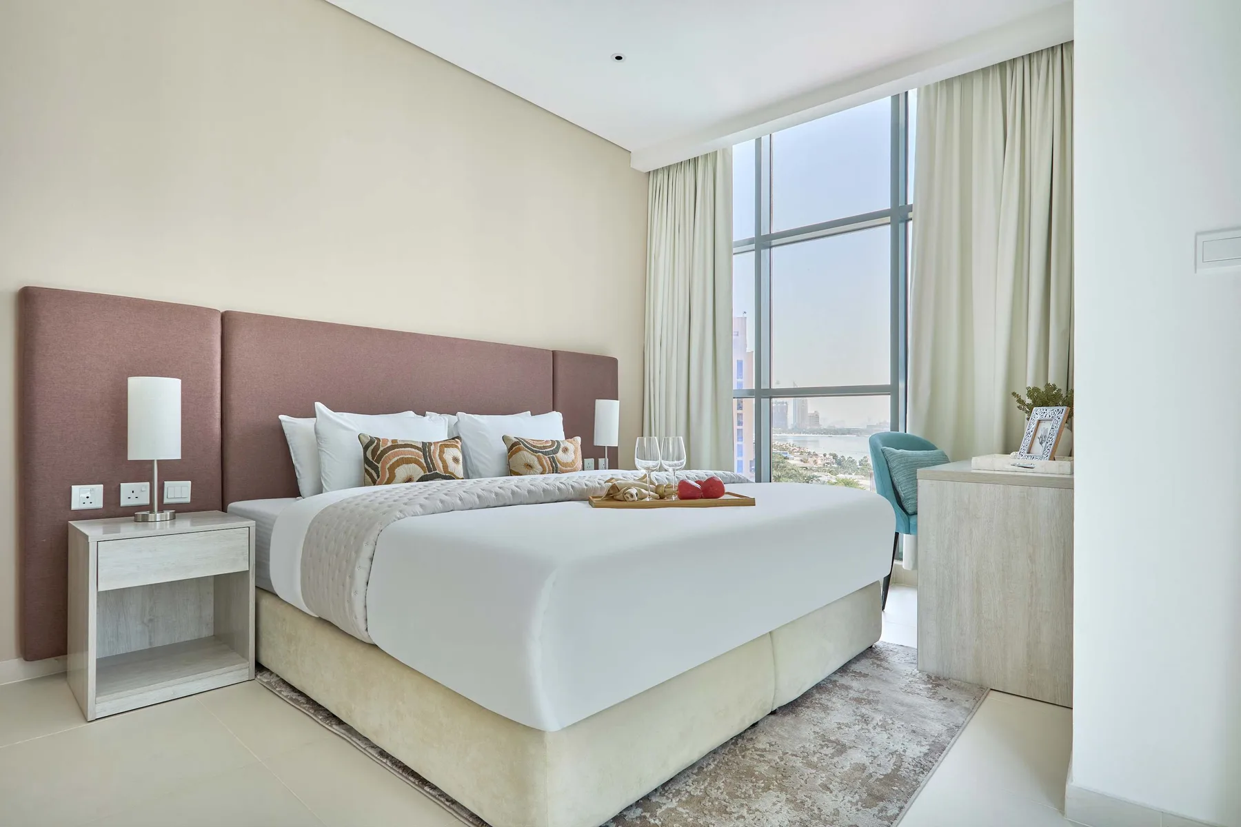 Un dormitorio con una cama bien tendida junto a una gran ventana con cortinas.
