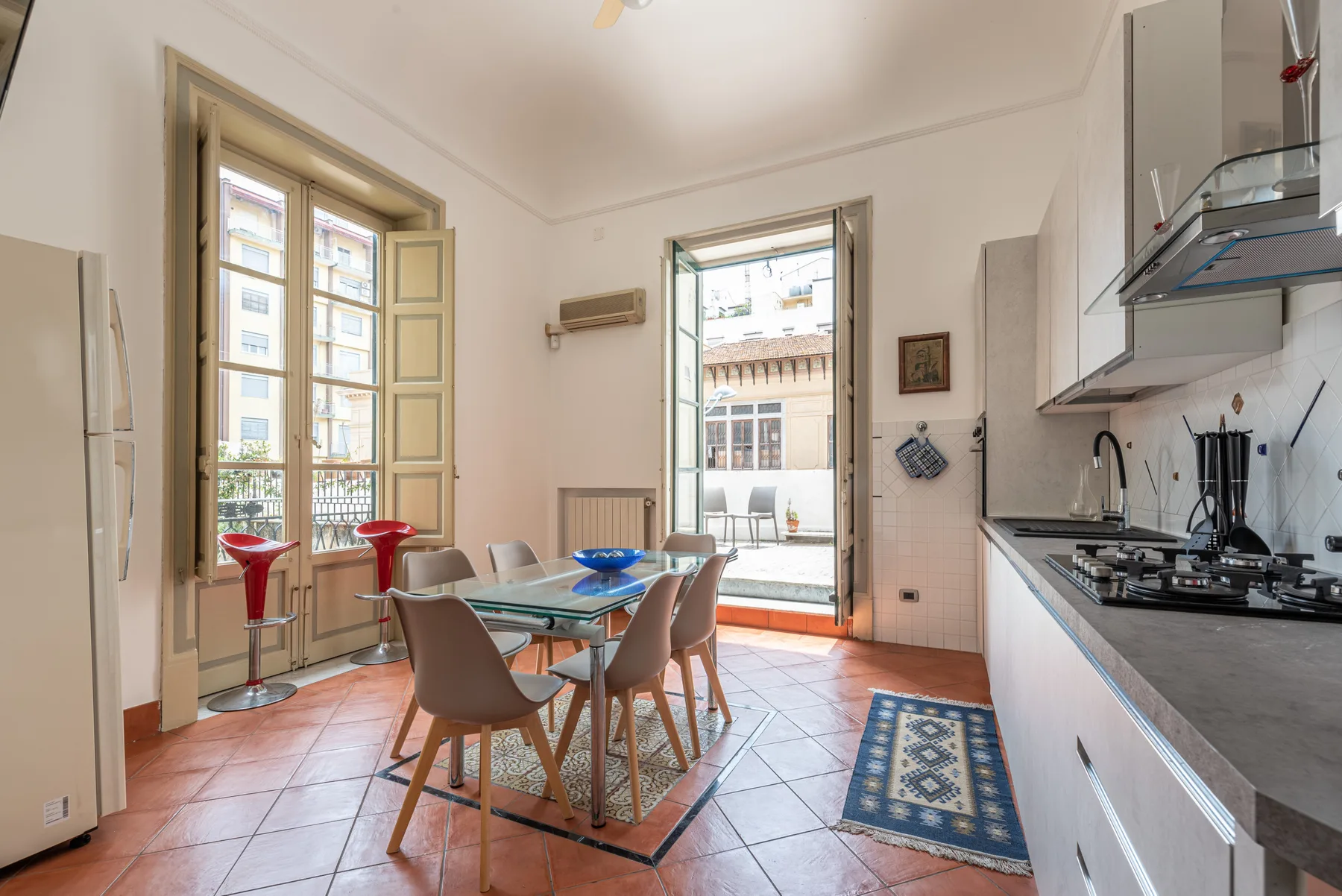 A bright kitchen and dining area with a glass table beside open balcony doors.
