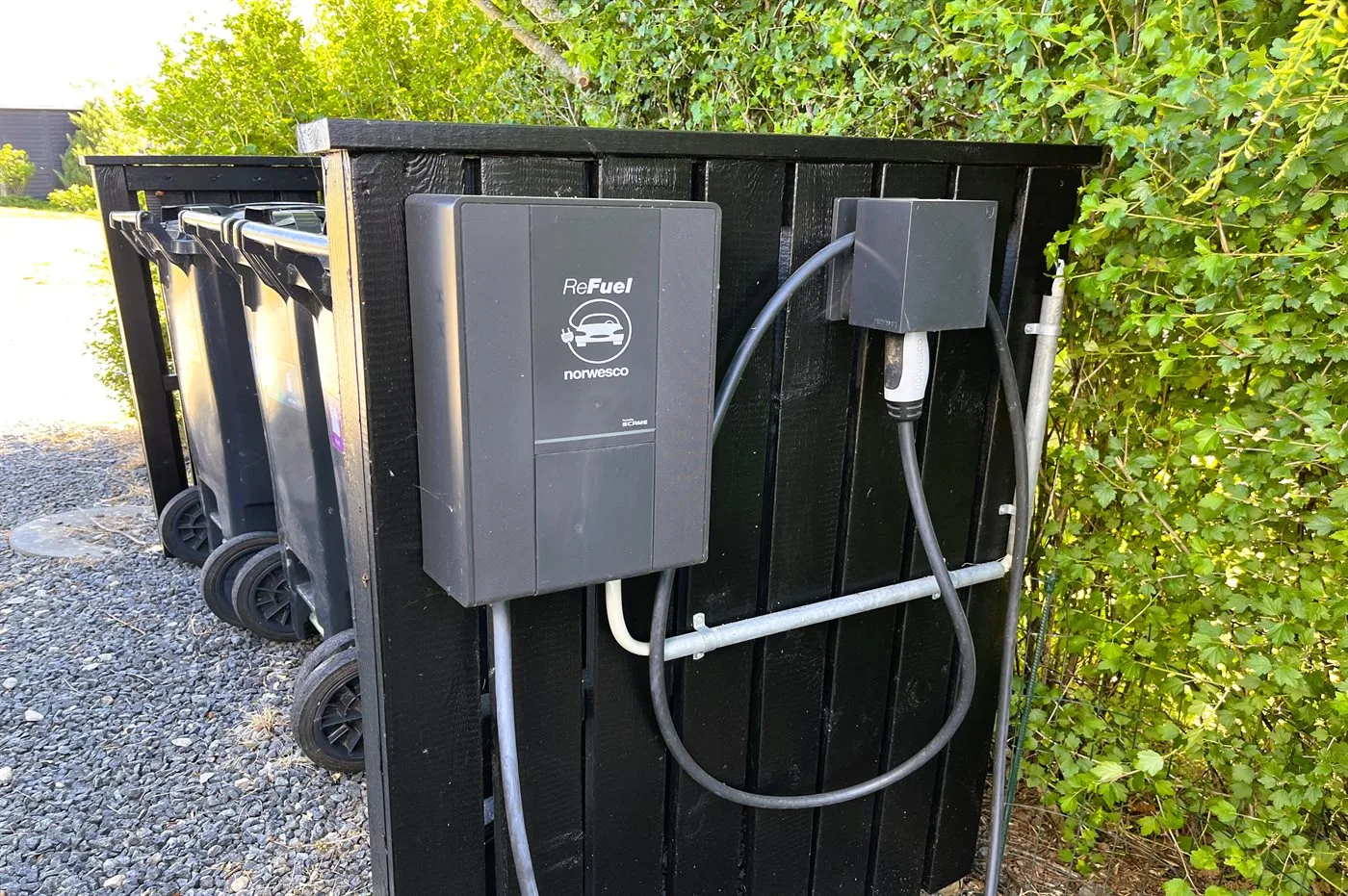 Cajas eléctricas y cables están montados en un recinto negro junto a contenedores con ruedas.