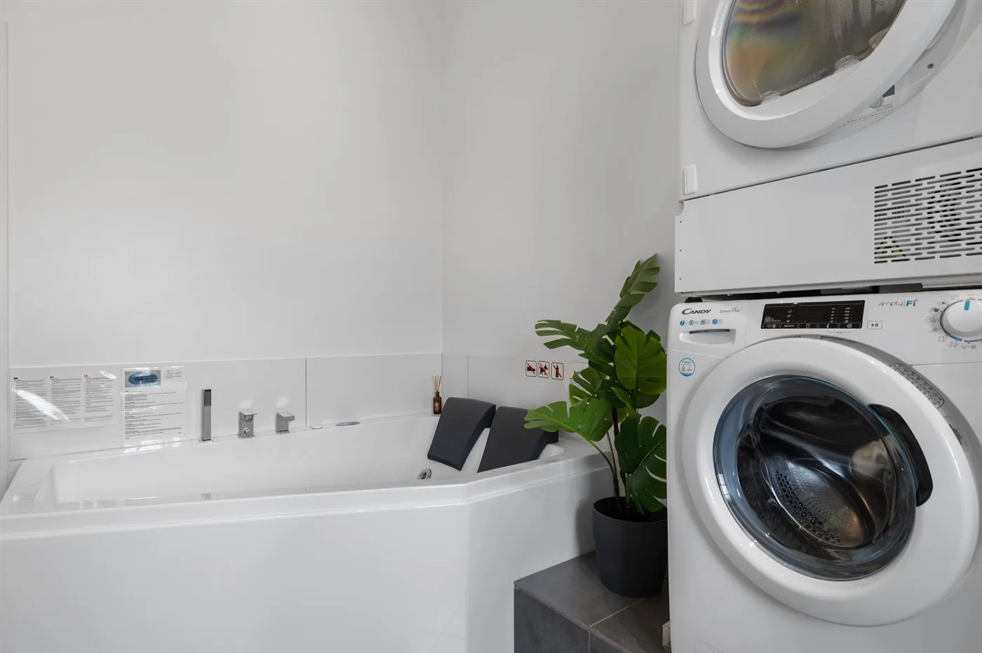 Un baño con una bañera junto a una lavadora y secadora apiladas.