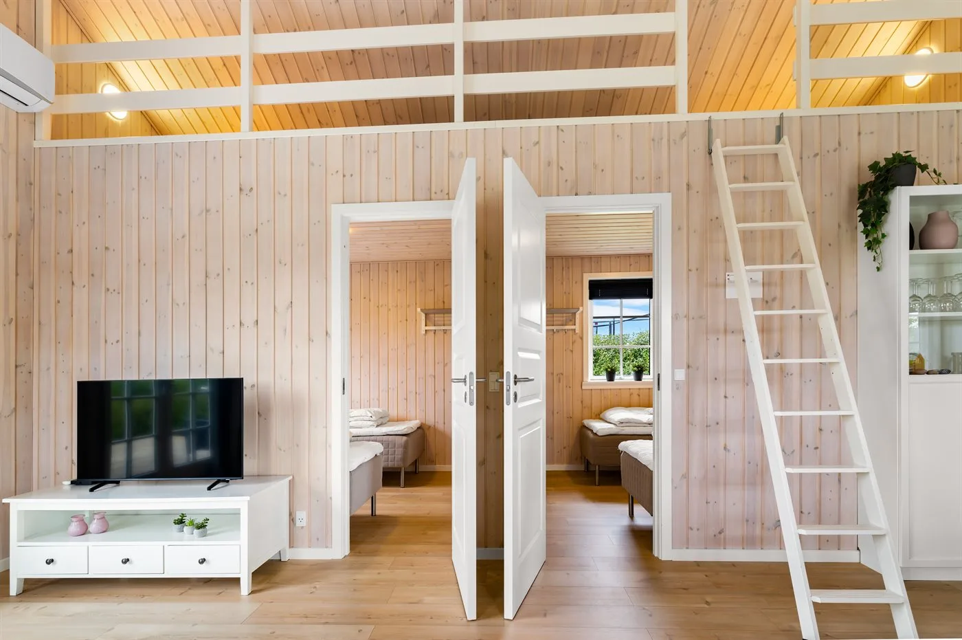Interior revestido de madera con dos puertas abiertas a dormitorios y un televisor.