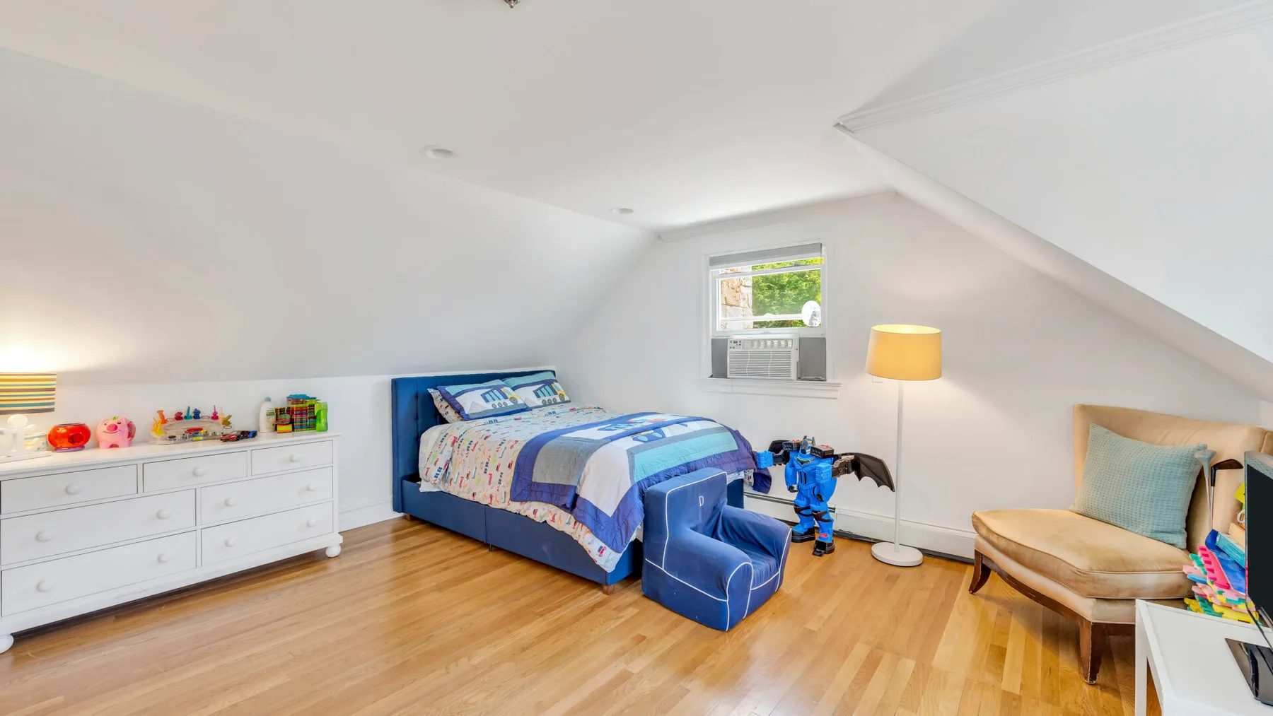 Un dormitorio abuhardillado luminoso con una cama azul y una cómoda blanca baja.