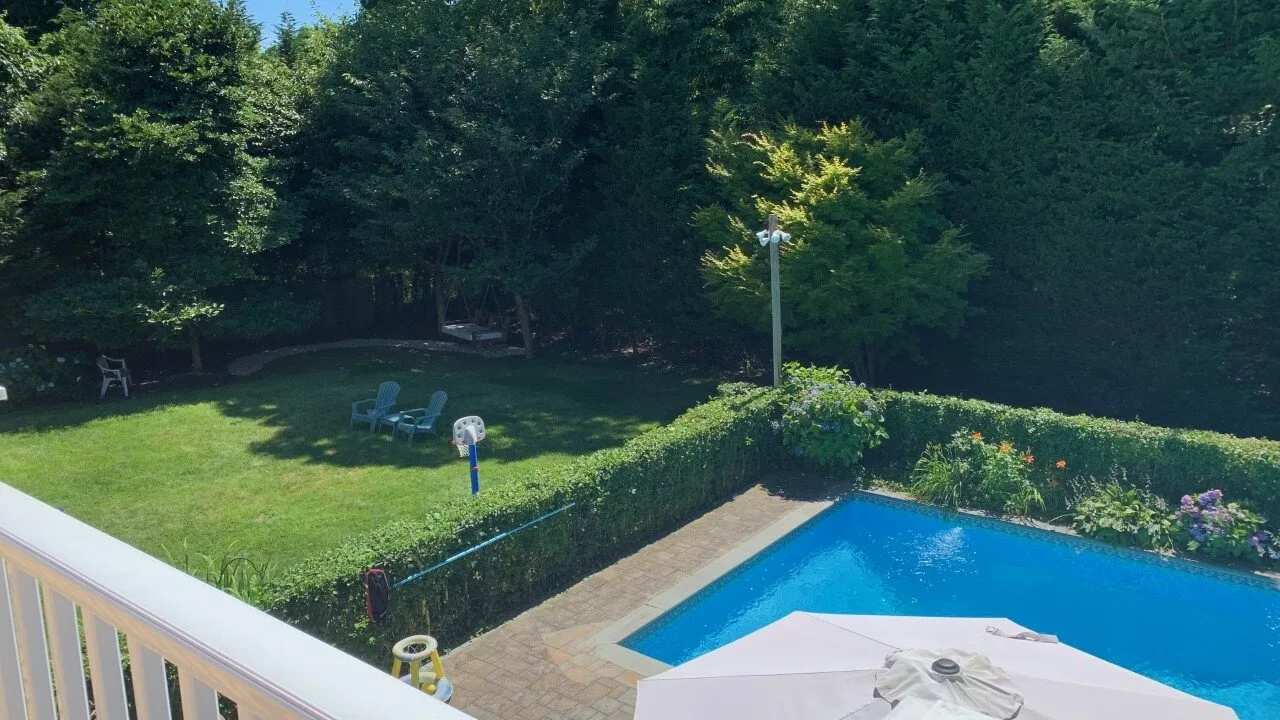 Una piscina está junto a un jardín con setos y un césped sombreado.