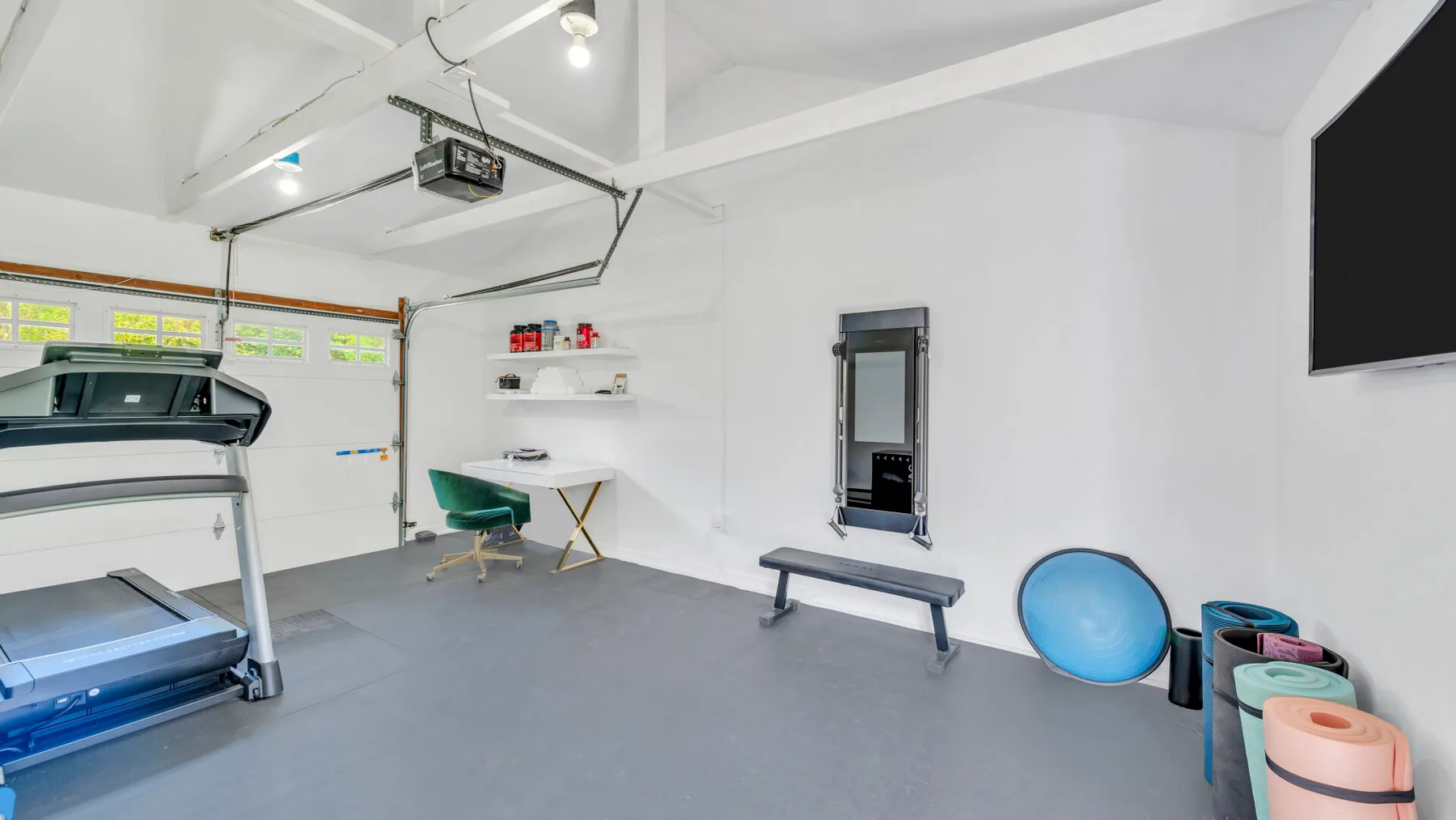 Un gimnasio en casa con equipo de ejercicio, un banco y una pantalla en la pared.
