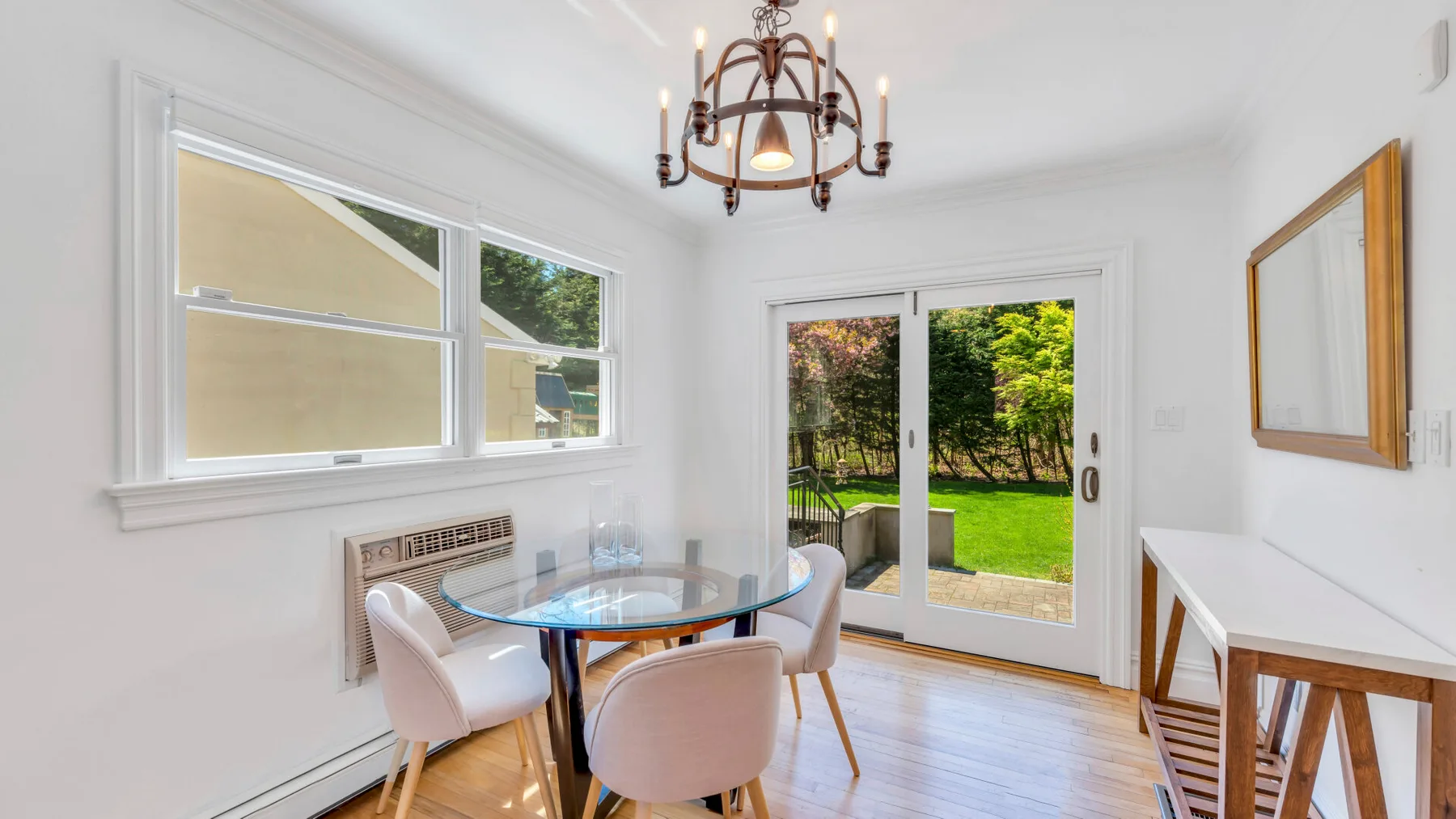 Un comedor luminoso con una mesa redonda junto a ventanas y puertas de vidrio que dan a un jardín.