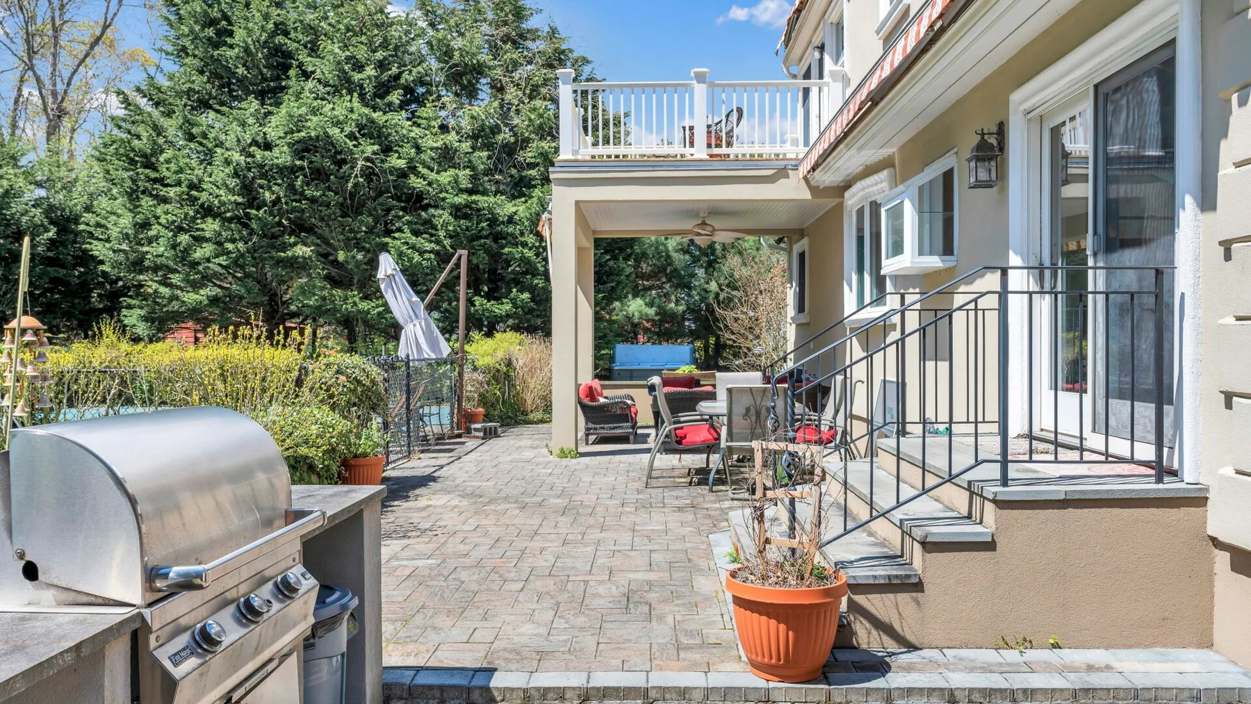 Un patio pavimentado junto a la casa tiene asientos y una parrilla.
