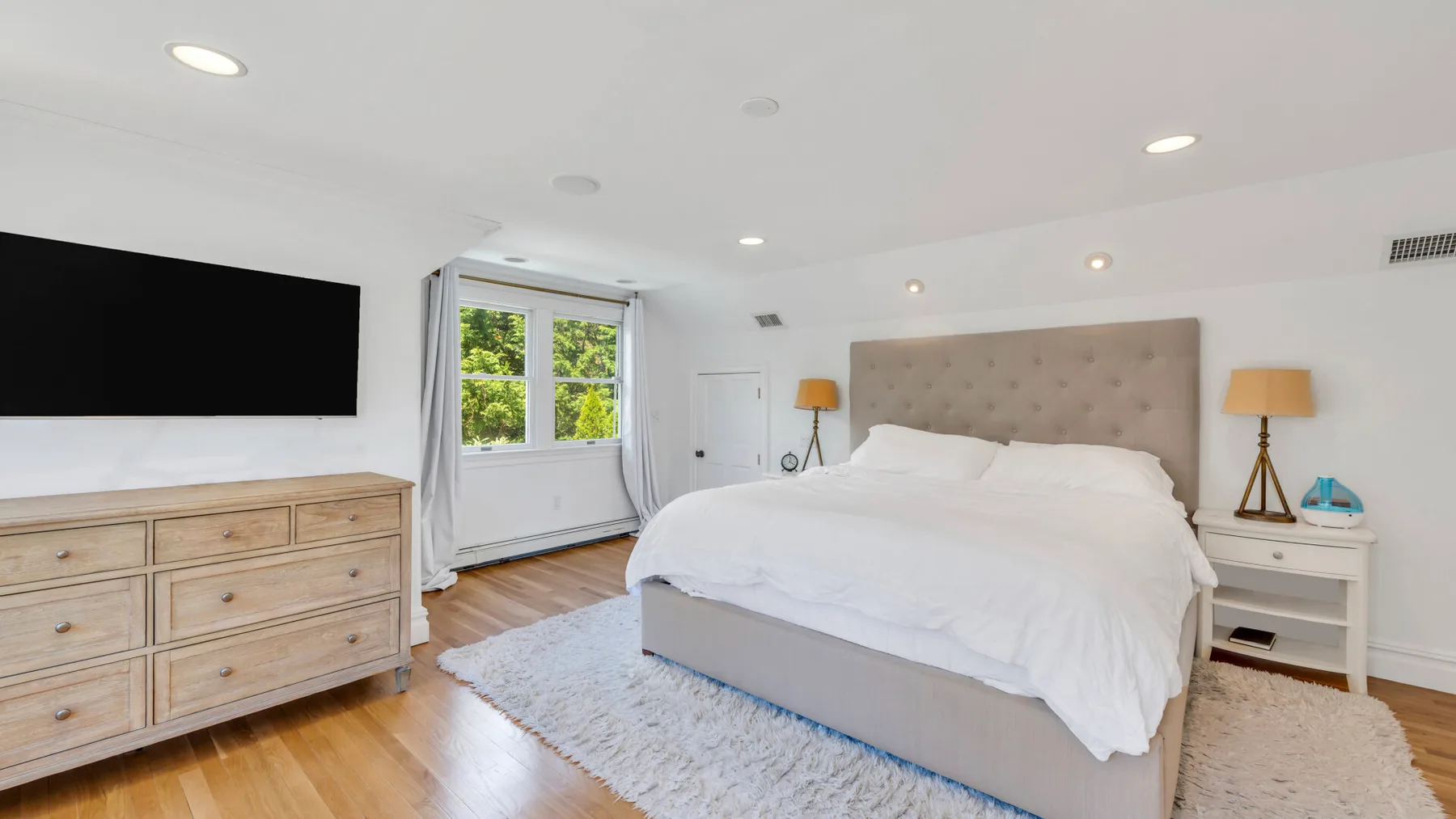 Un dormitorio luminoso con una cama grande, mesitas de noche y un televisor.