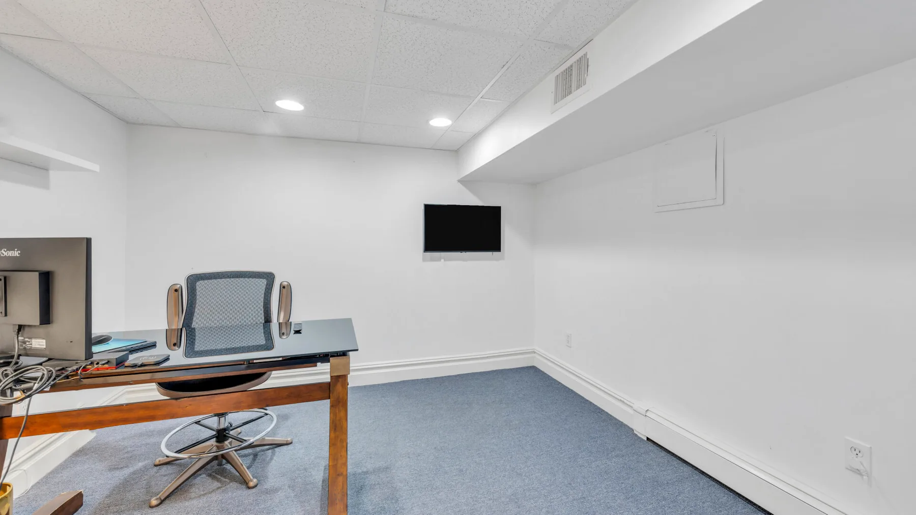 Un espacio de trabajo con escritorio y silla está en una habitación luminosa con alfombra.