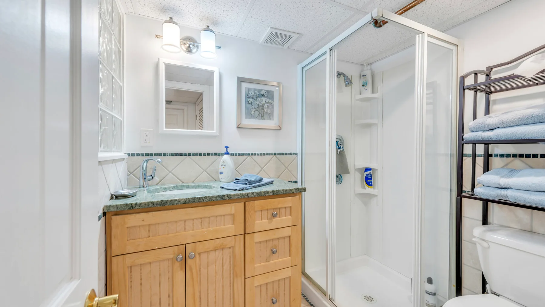 Un baño luminoso con lavabo, mueble y ducha con mampara de vidrio.