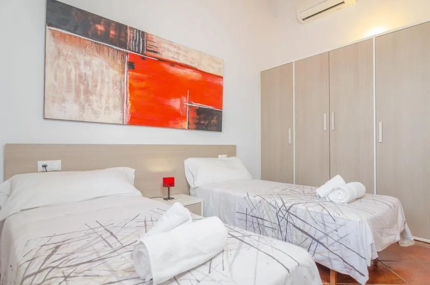 Un dormitorio luminoso con dos camas, armarios claros y arte abstracto colorido en la pared.