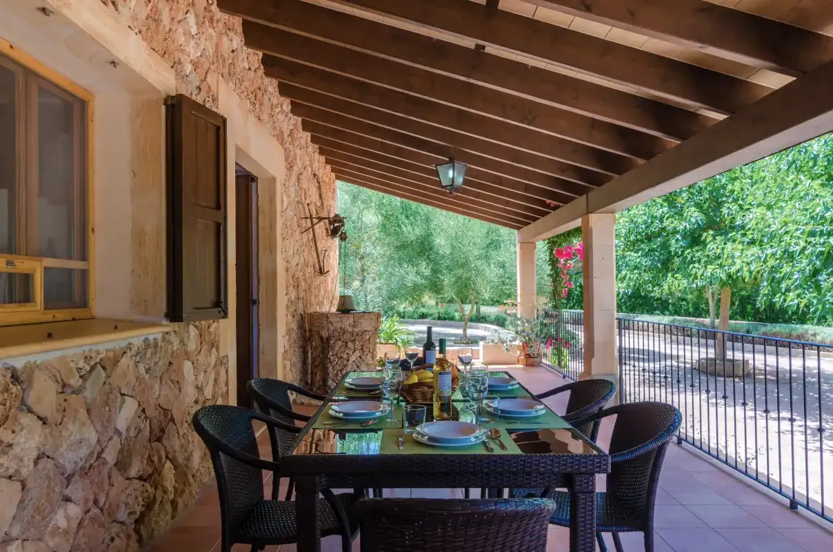 Comedor exterior cubierto con una mesa larga y asientos junto a una pared de piedra.