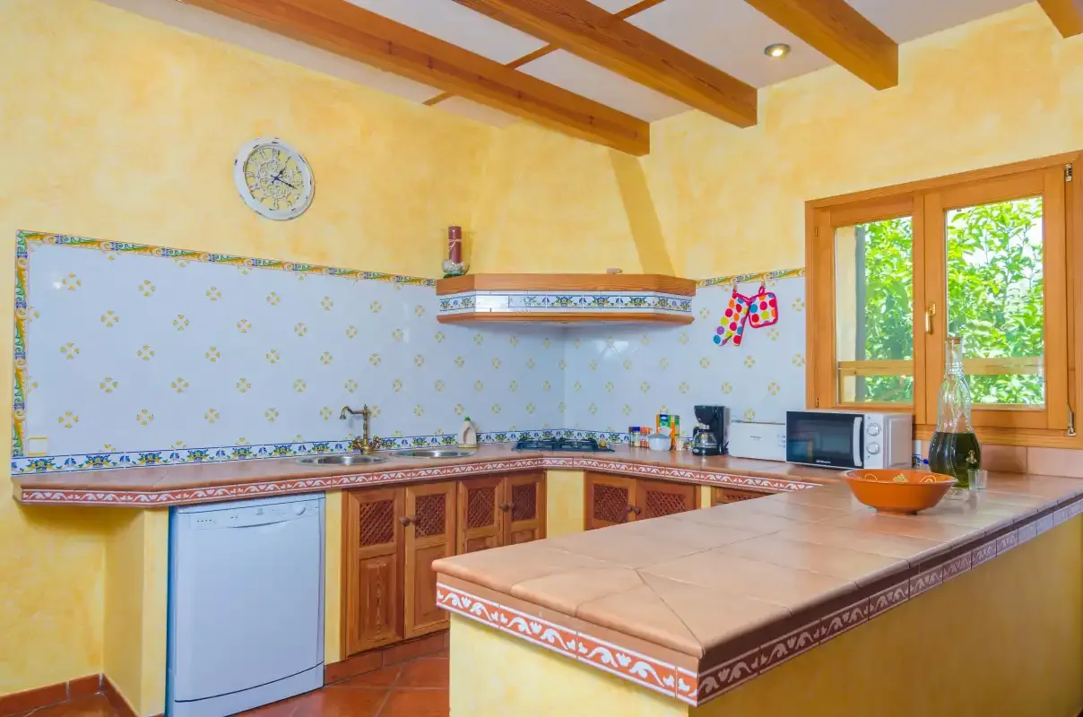Una cocina luminosa con encimeras de azulejos, armarios de madera y una ventana con vistas a la vegetación.