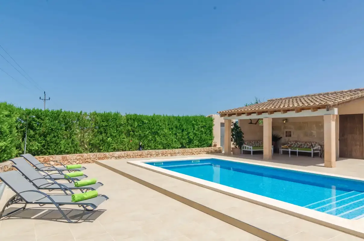 Una piscina al aire libre junto a un patio cubierto y varias tumbonas.