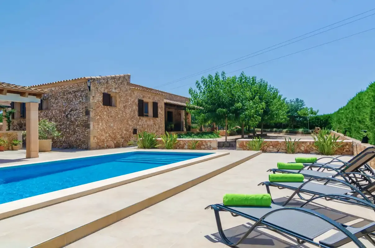 Una casa de piedra y una piscina al aire libre con asientos para descansar.