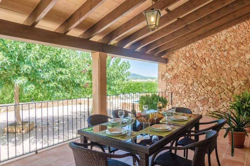 Una zona de comedor exterior cubierta tiene una mesa y asientos junto a una pared de piedra.