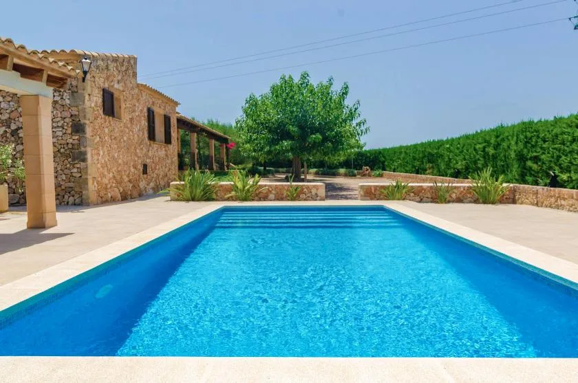 An outdoor swimming pool beside a stone building and landscaped grounds.
