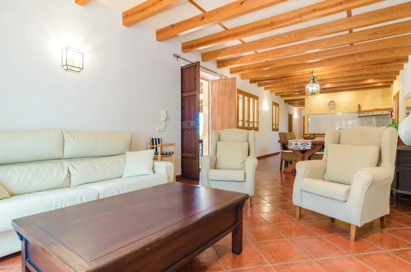 Una sala de estar con asientos claros, una mesa de centro de madera y vigas expuestas.