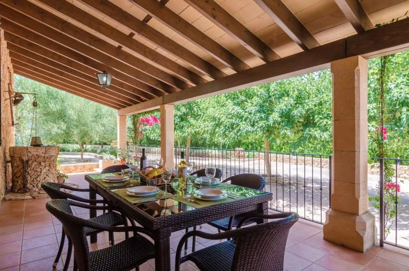 Comedor exterior cubierto con una mesa y asientos frente a un jardín.