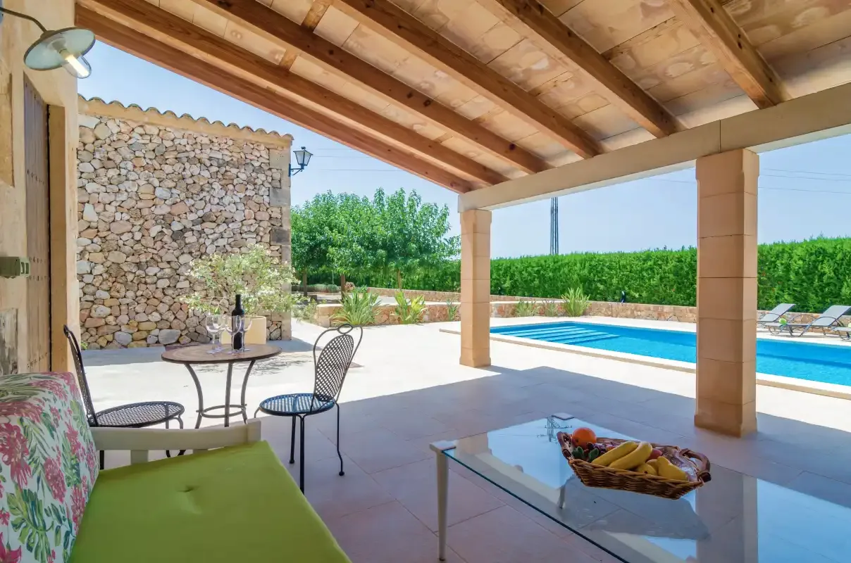 Un patio cubierto con asientos da a una piscina y un jardín.