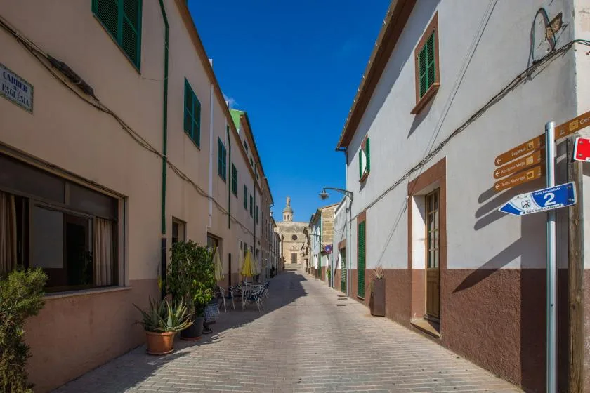 Una calle estrecha pavimentada pasa entre edificios, con señales en un poste de esquina.