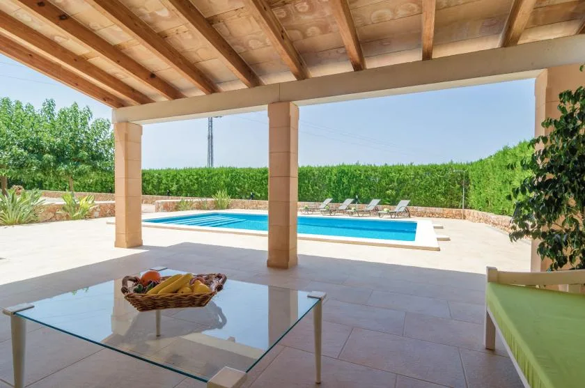 A covered patio overlooks a swimming pool and landscaped greenery.