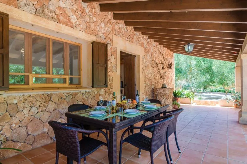 Un patio cubierto de piedra con una mesa de comedor y vegetación al fondo.