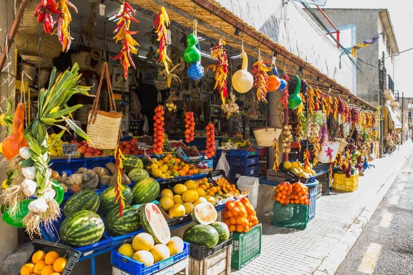 Un puesto de mercado al aire libre exhibe frutas, verduras y chiles colgantes.