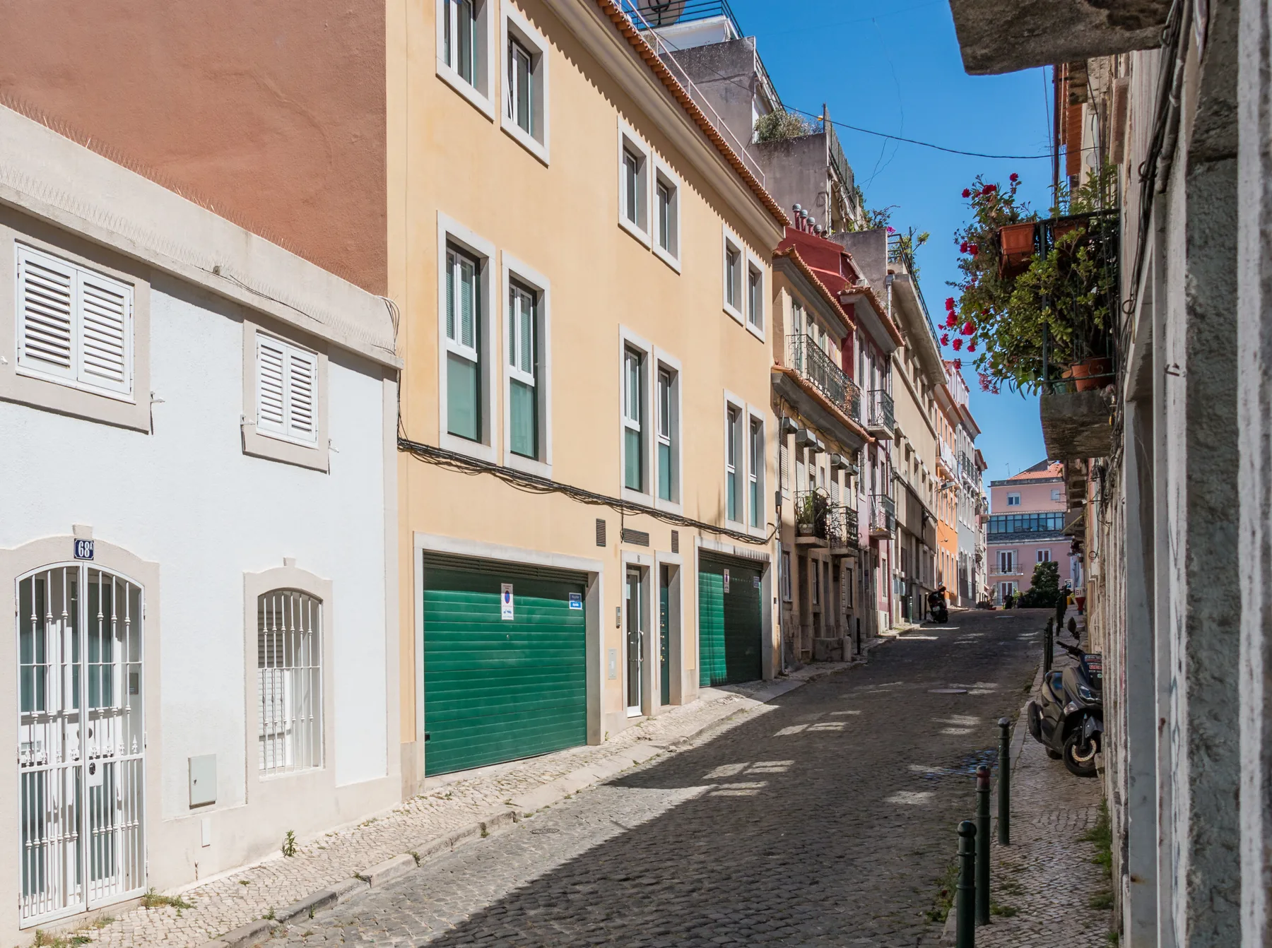 A narrow cobblestone street lined with buildings and parked scooters.