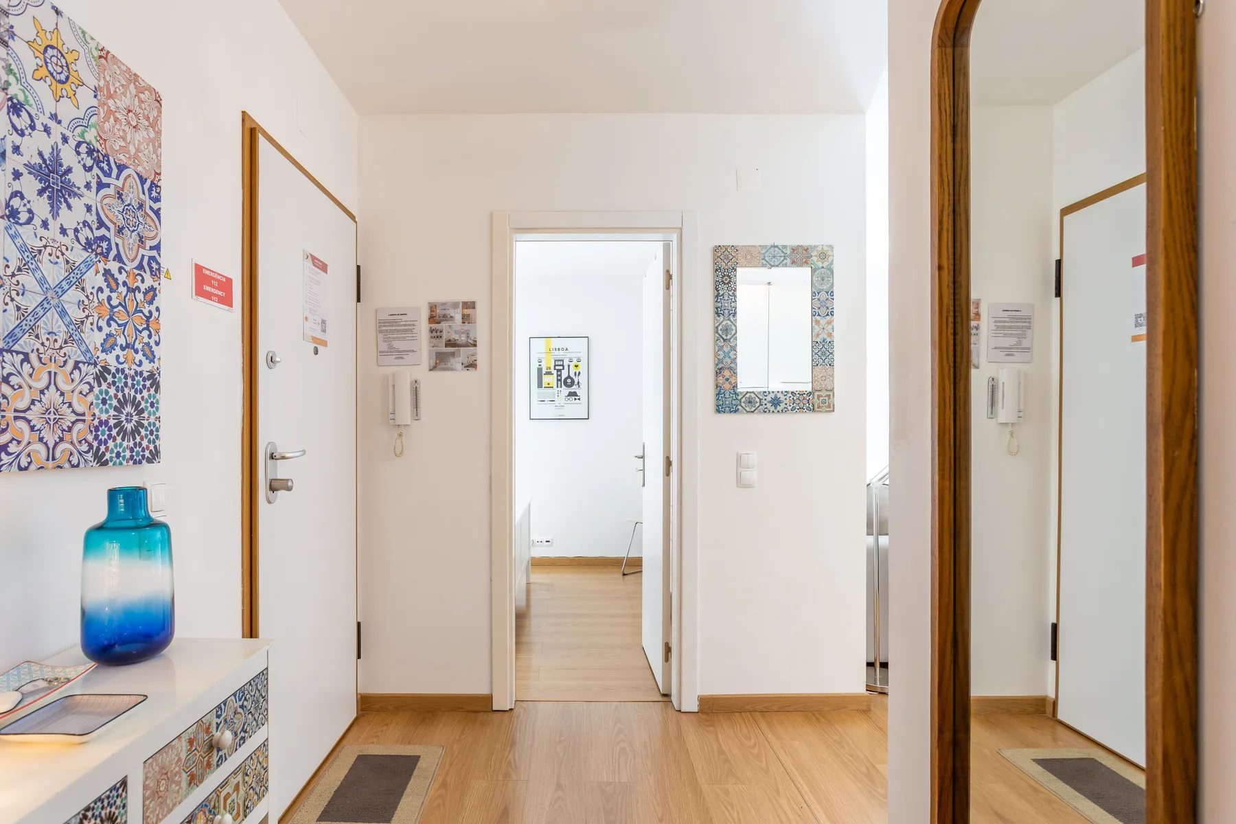 A bright apartment hallway with a tiled accent wall and wooden flooring.