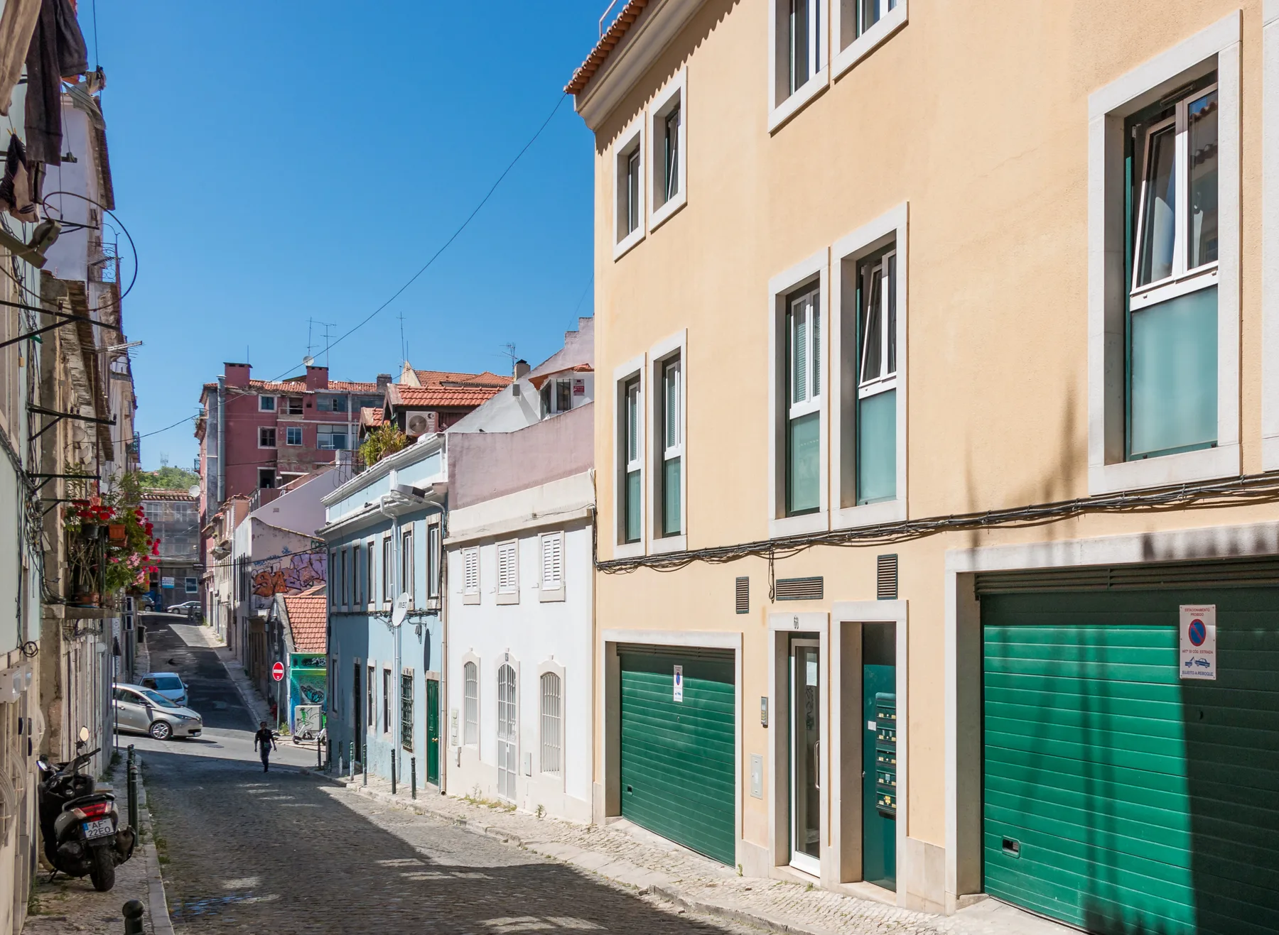 A narrow cobblestone street lined with colorful buildings and parked vehicles.