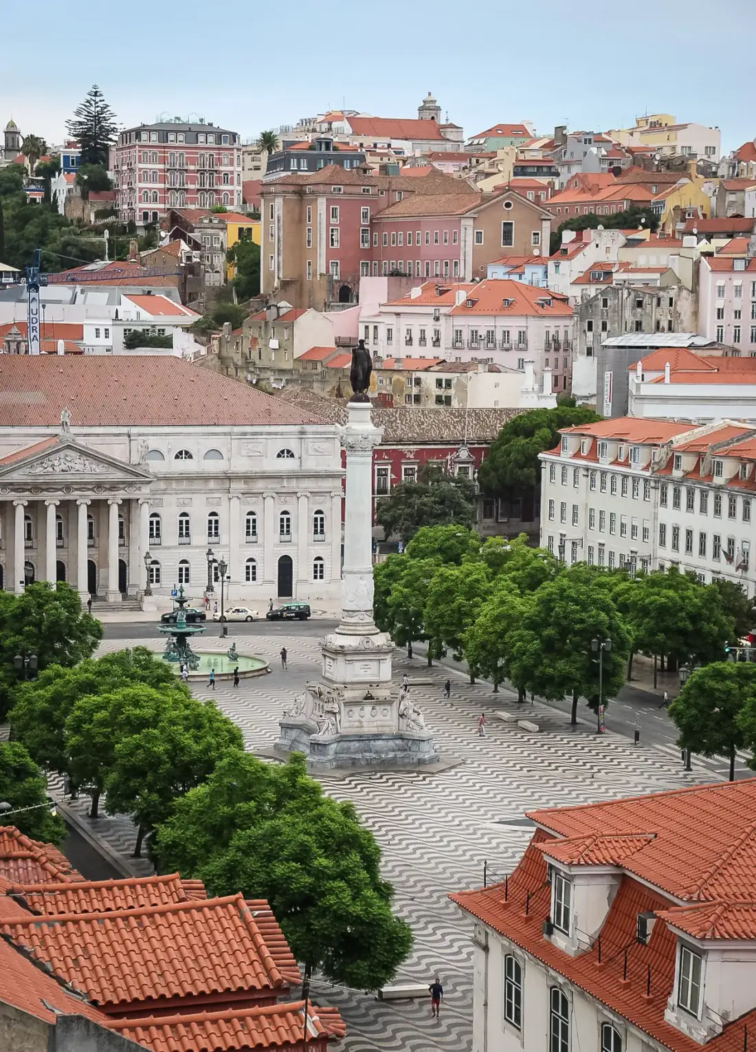 A city square with patterned paving, trees, and surrounding buildings.