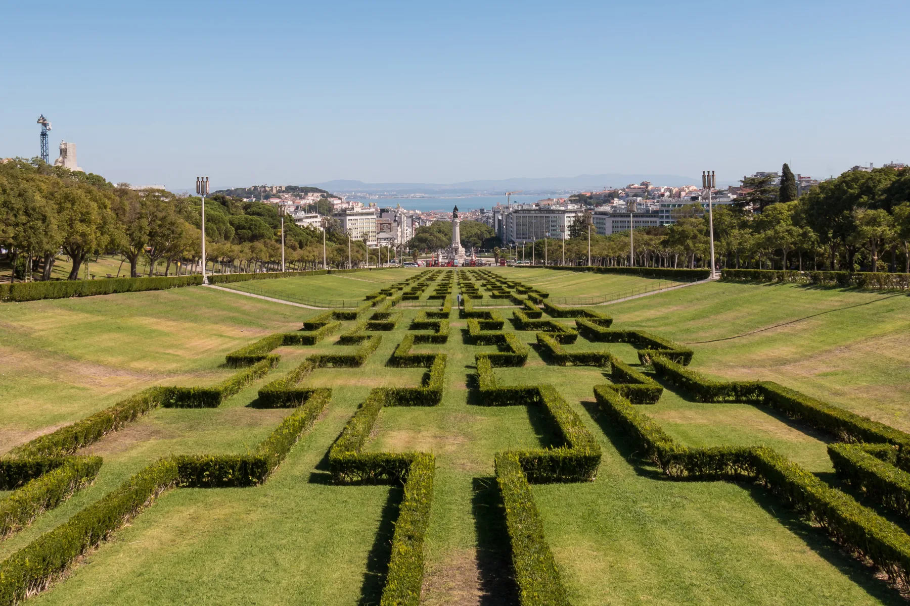 A formal garden with geometric hedges stretches toward the city skyline.