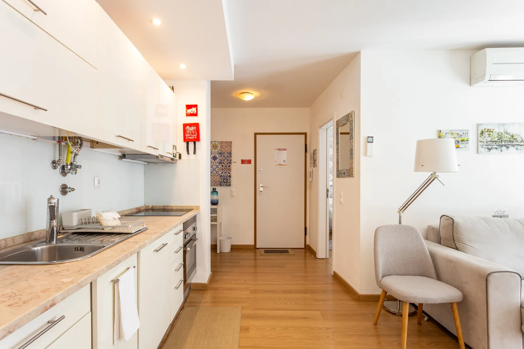 A bright apartment interior with a kitchenette and a seating area along the hallway.