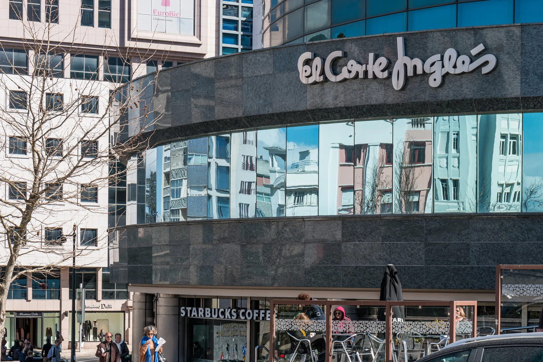 A city shopping center with a large El Corte Inglés sign and storefronts at street level.