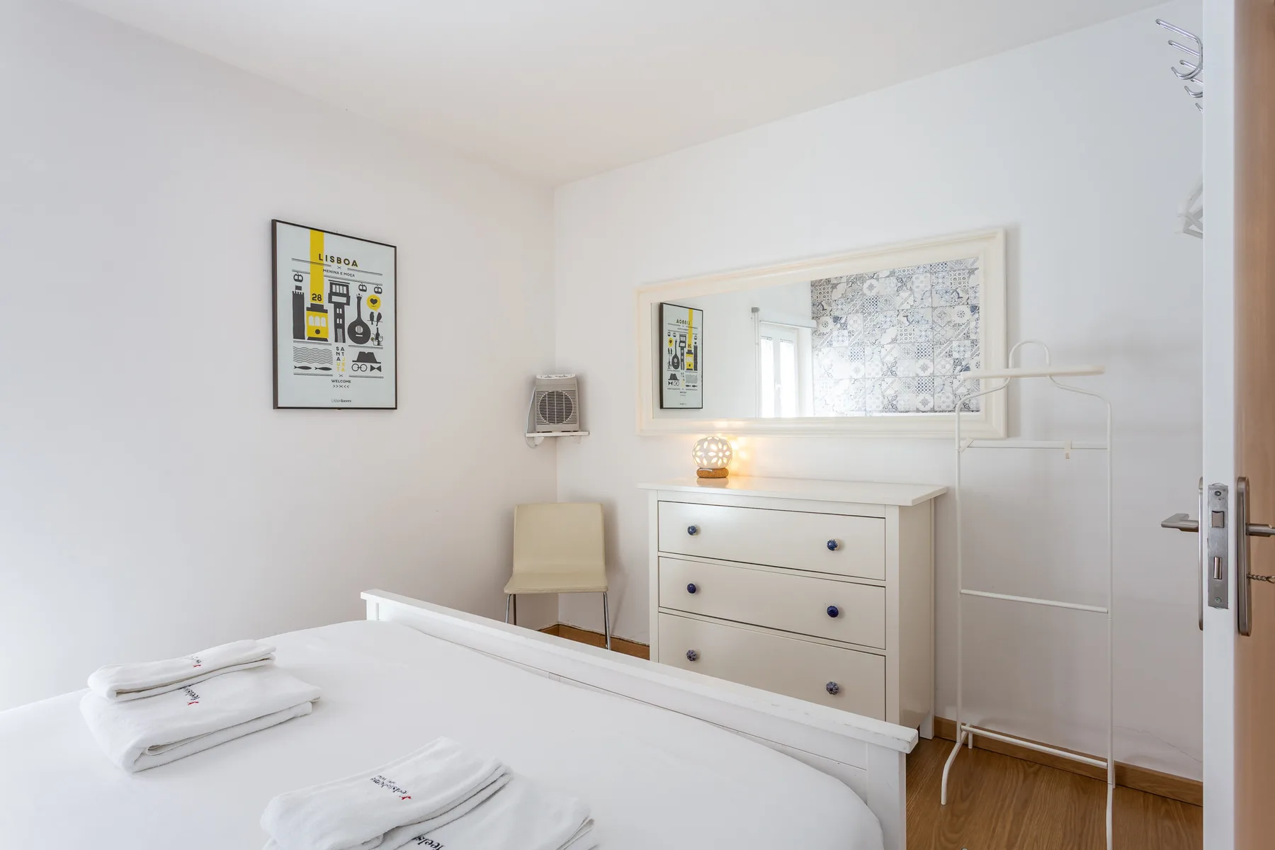 A bright bedroom with a white bed, dresser, and wall mirror.