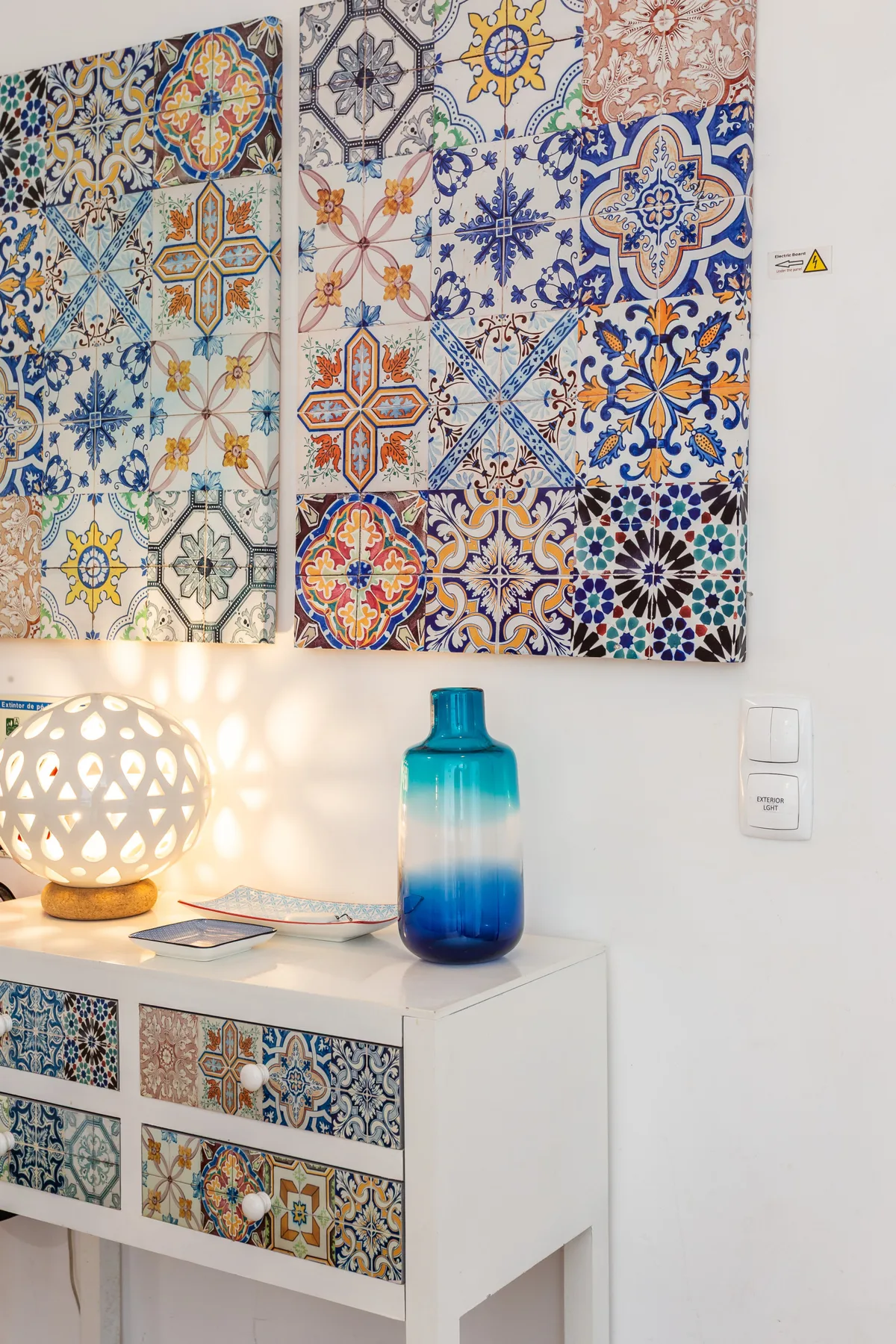 A decorated interior wall with colorful patterned tiles above a white cabinet.