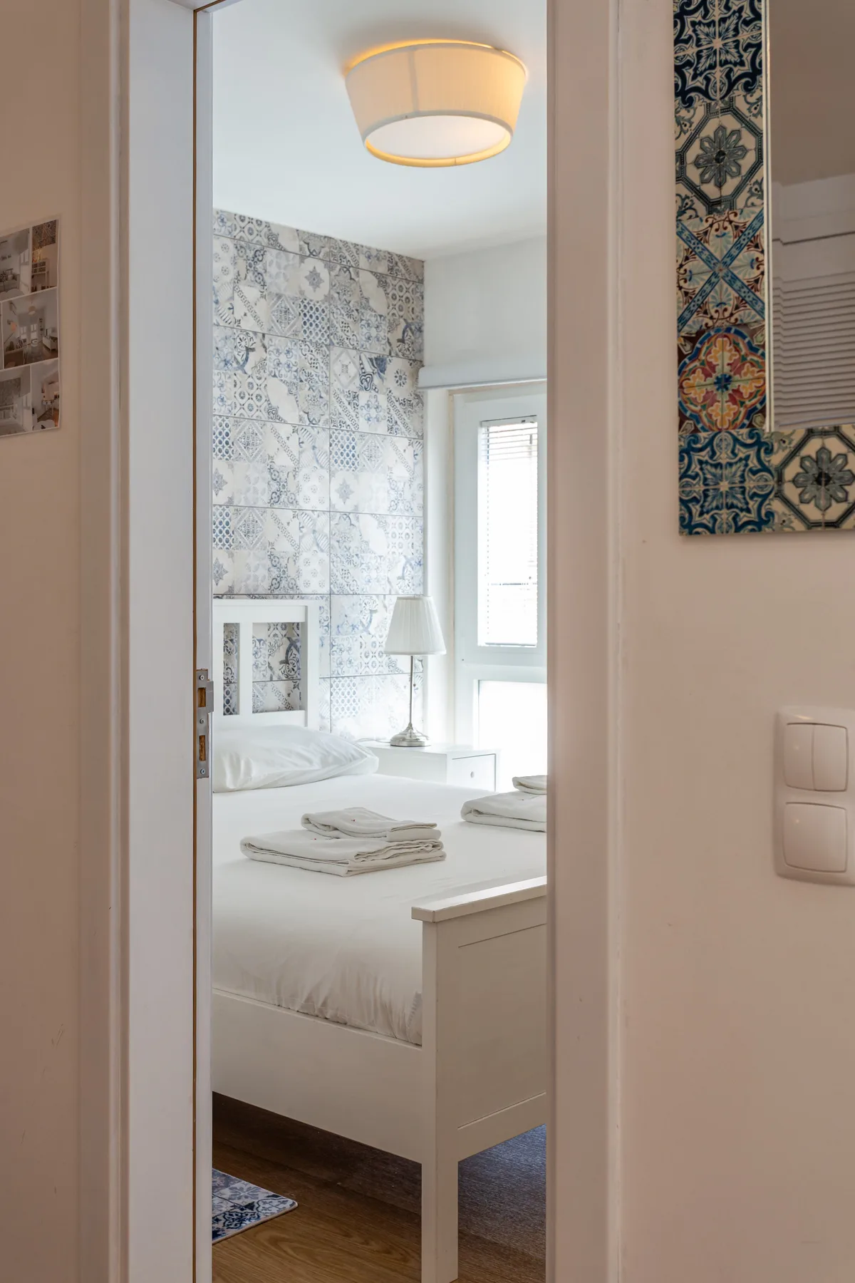 A bedroom with a white bed and patterned tile wall.