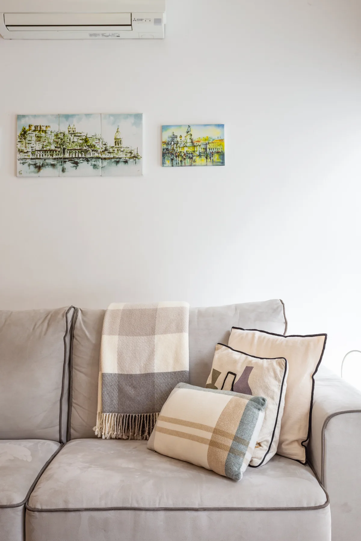 A living room with a light-colored sofa, patterned cushions, and framed artwork.
