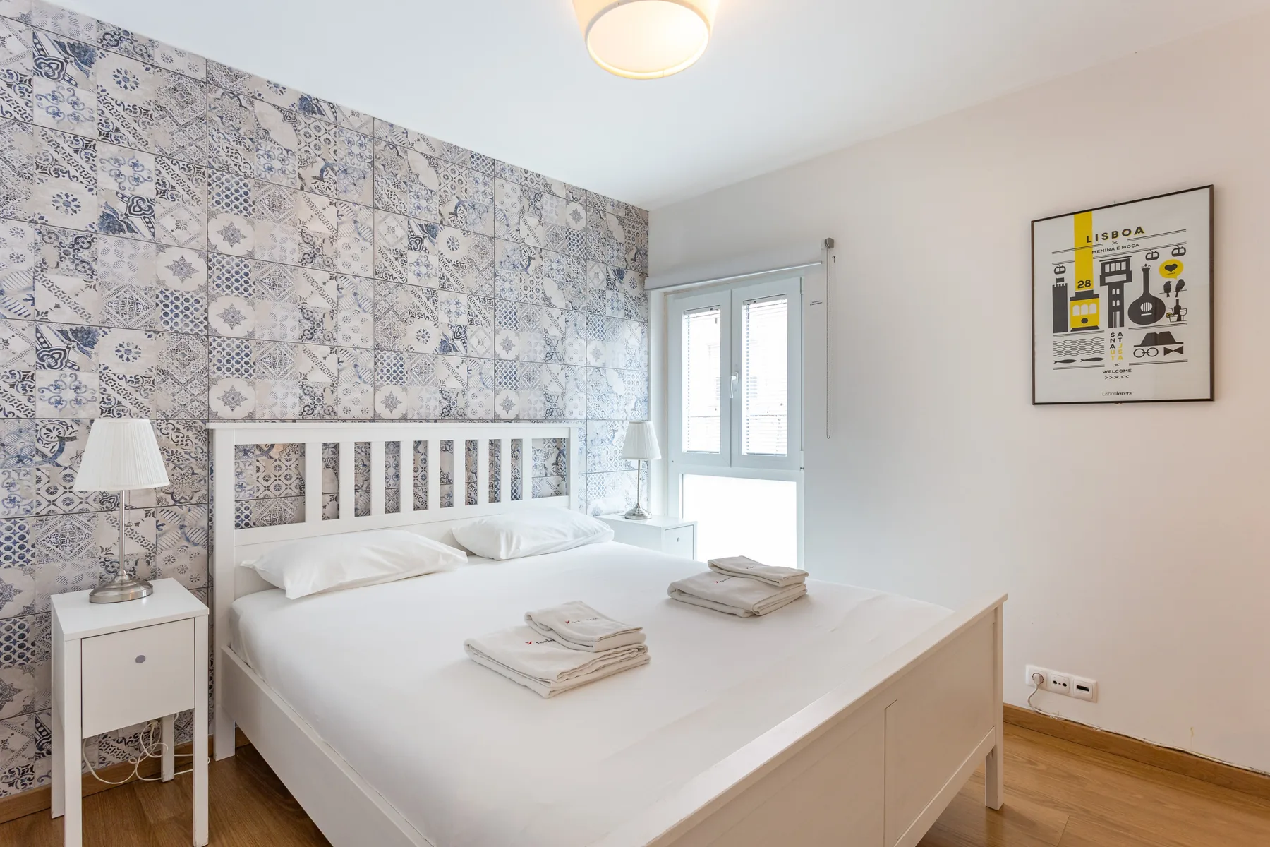 A bedroom with a white bed, patterned tile wall, and window.