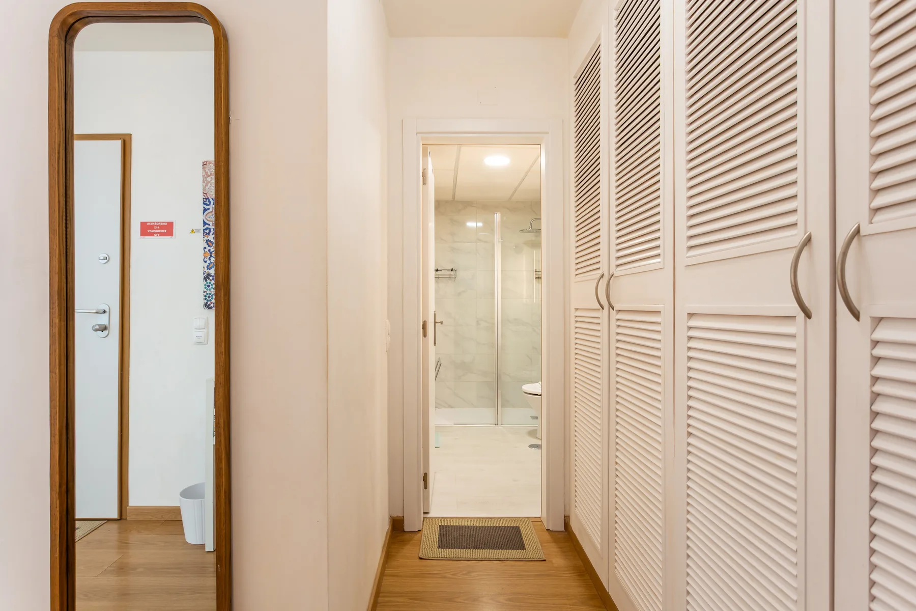 A hallway with mirrored doors and a bathroom visible at the end.