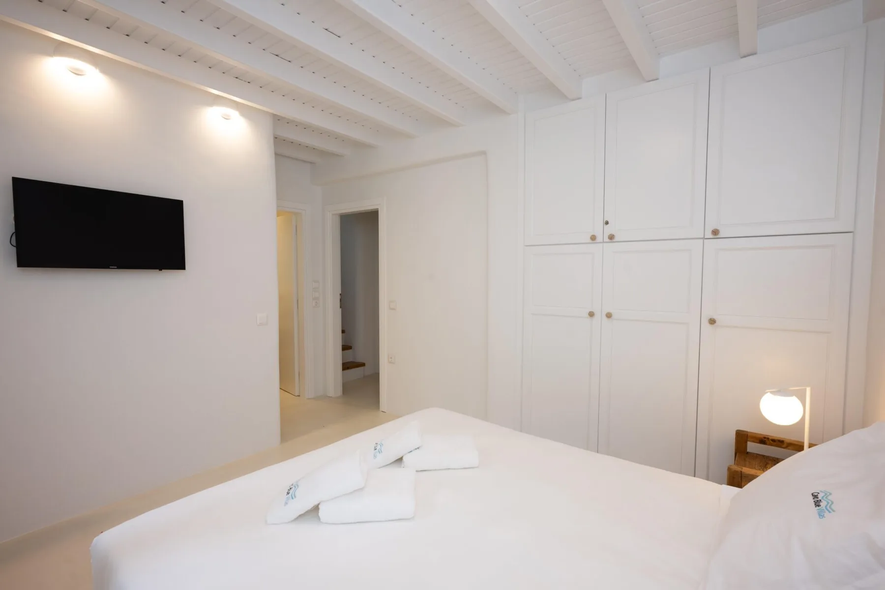 Un dormitorio con ropa de cama blanca, armarios empotrados y un televisor en la pared.