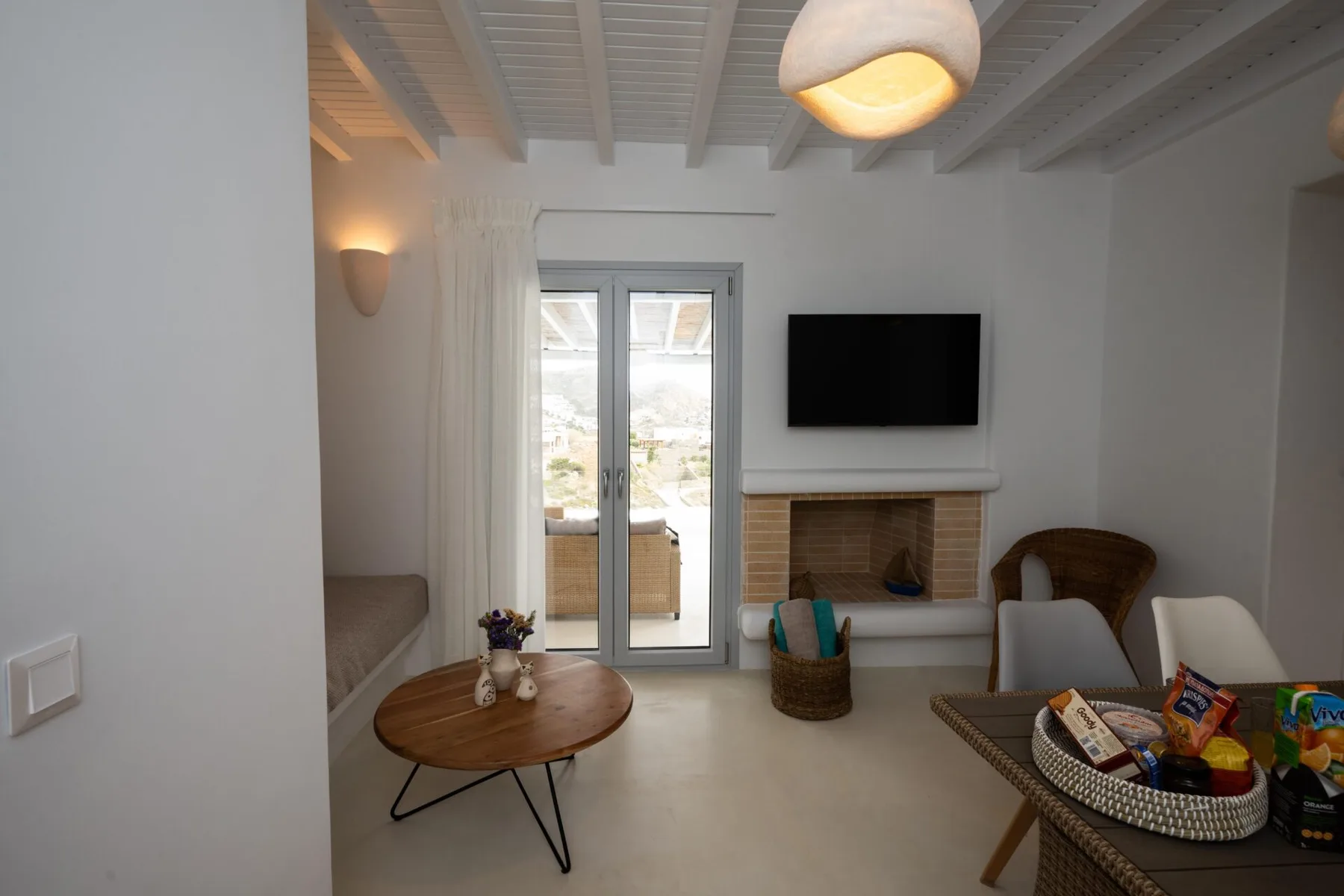 A living room with a television above a fireplace and doors opening to a balcony.